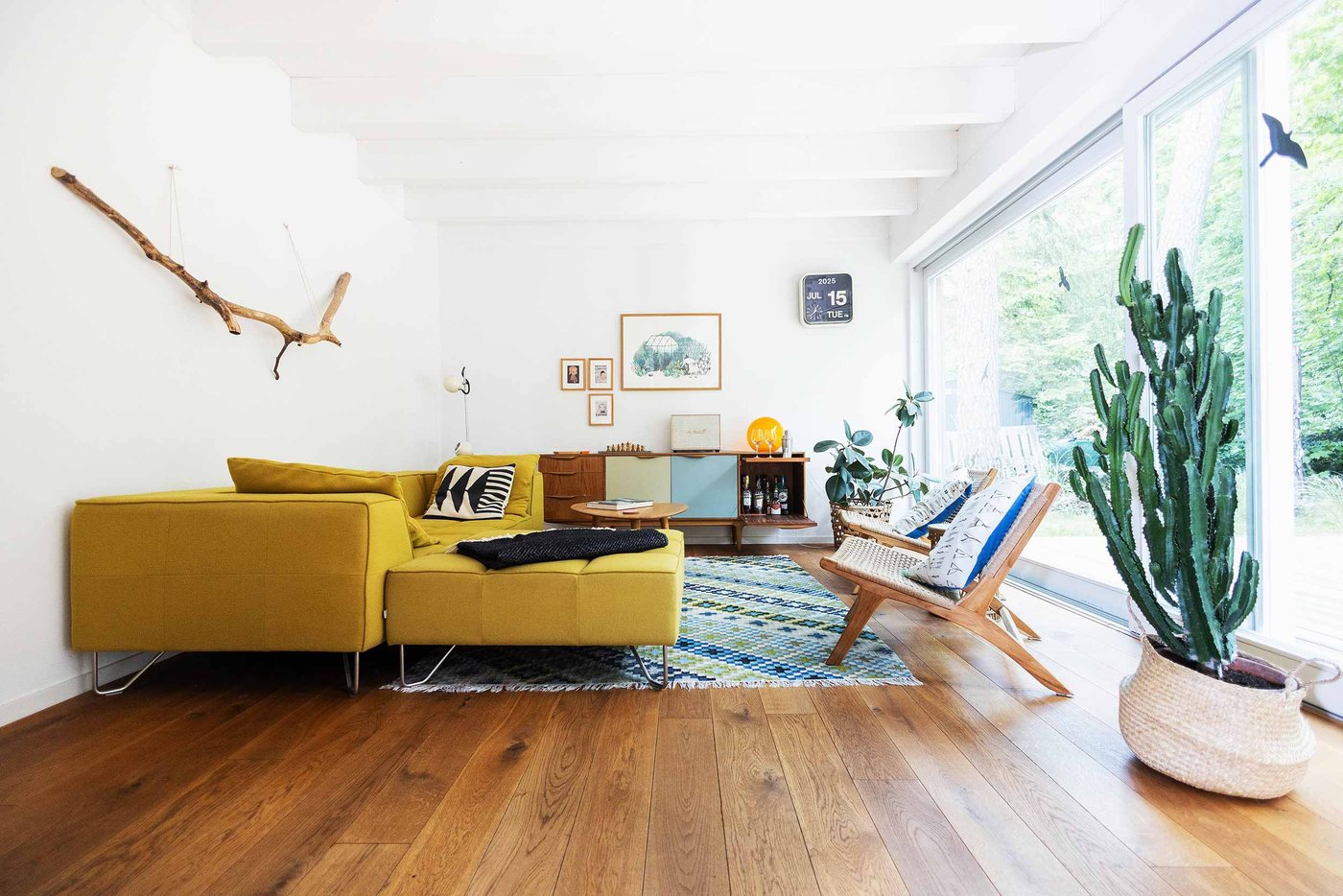 Holzhaus: Wohnzimmer mit gelbem Sofa, Kelim-Teppich und raumhohem Fenster zum Wald