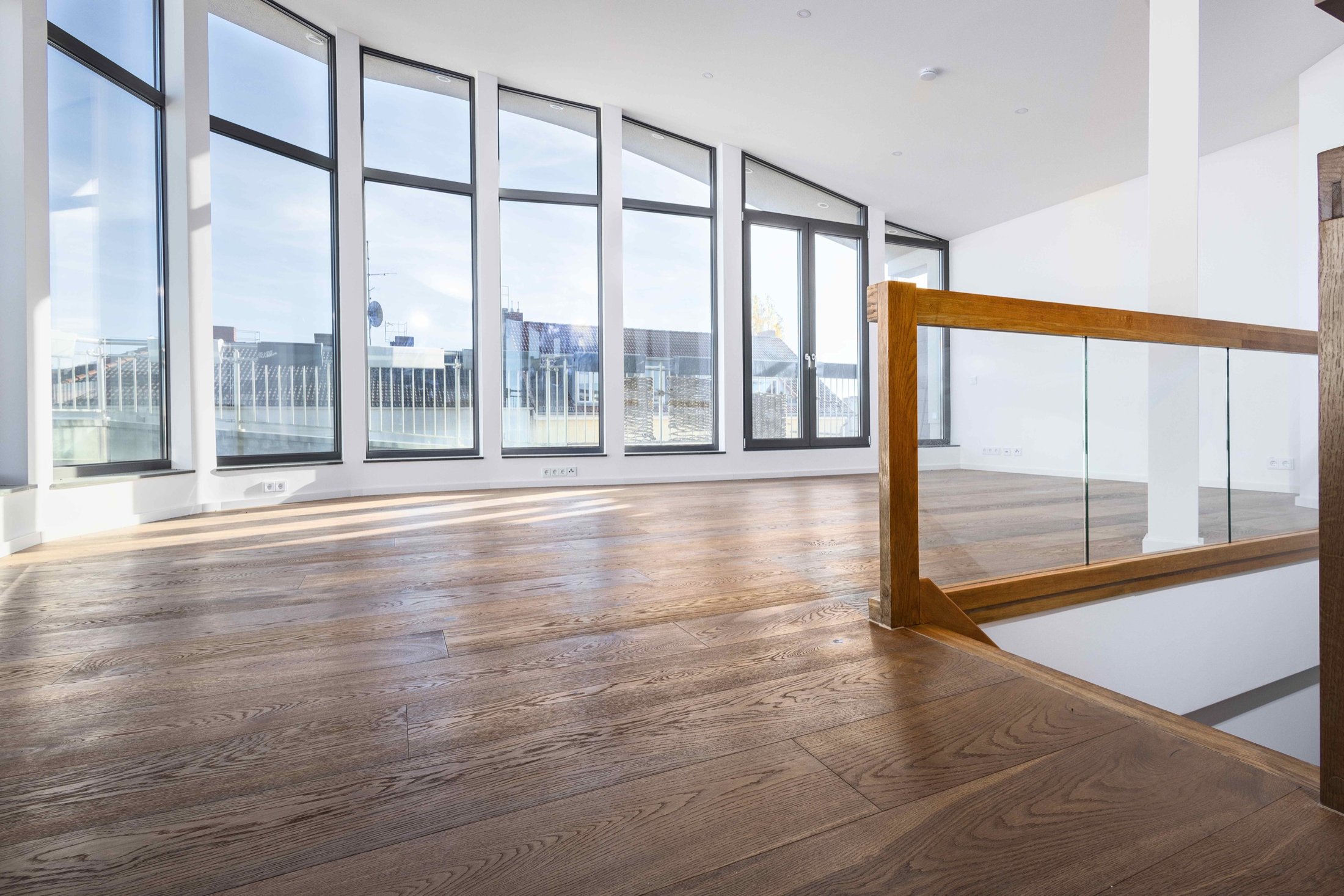 Wohnbereich mit geschwungener Fensterfront, Eichendielen und Glasgeländer, Projekt Leible & Cie.
