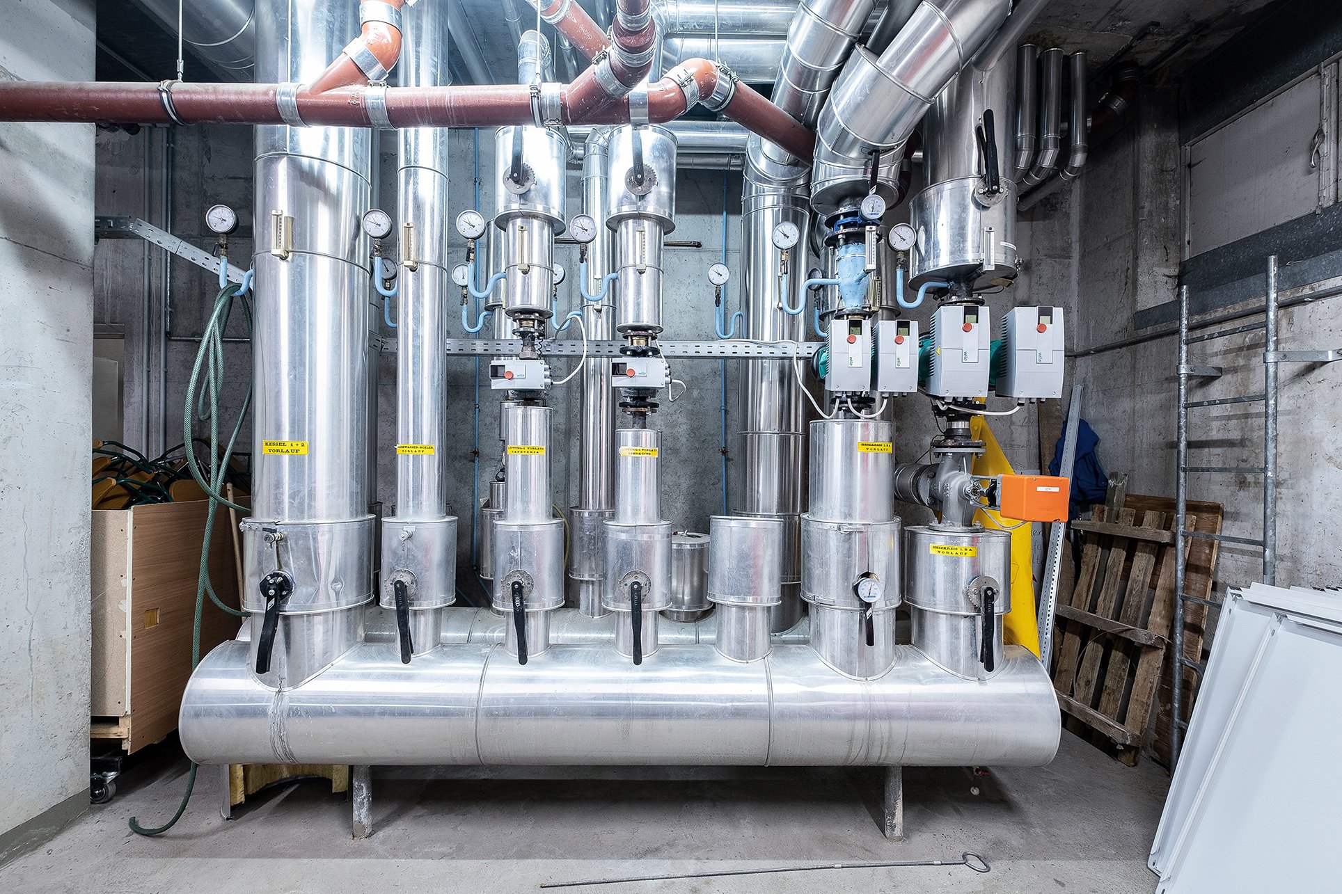 Heizungsverteiler mit isolierten Rohrleitungen und Pumpen im Technikraum, Projekt DENA