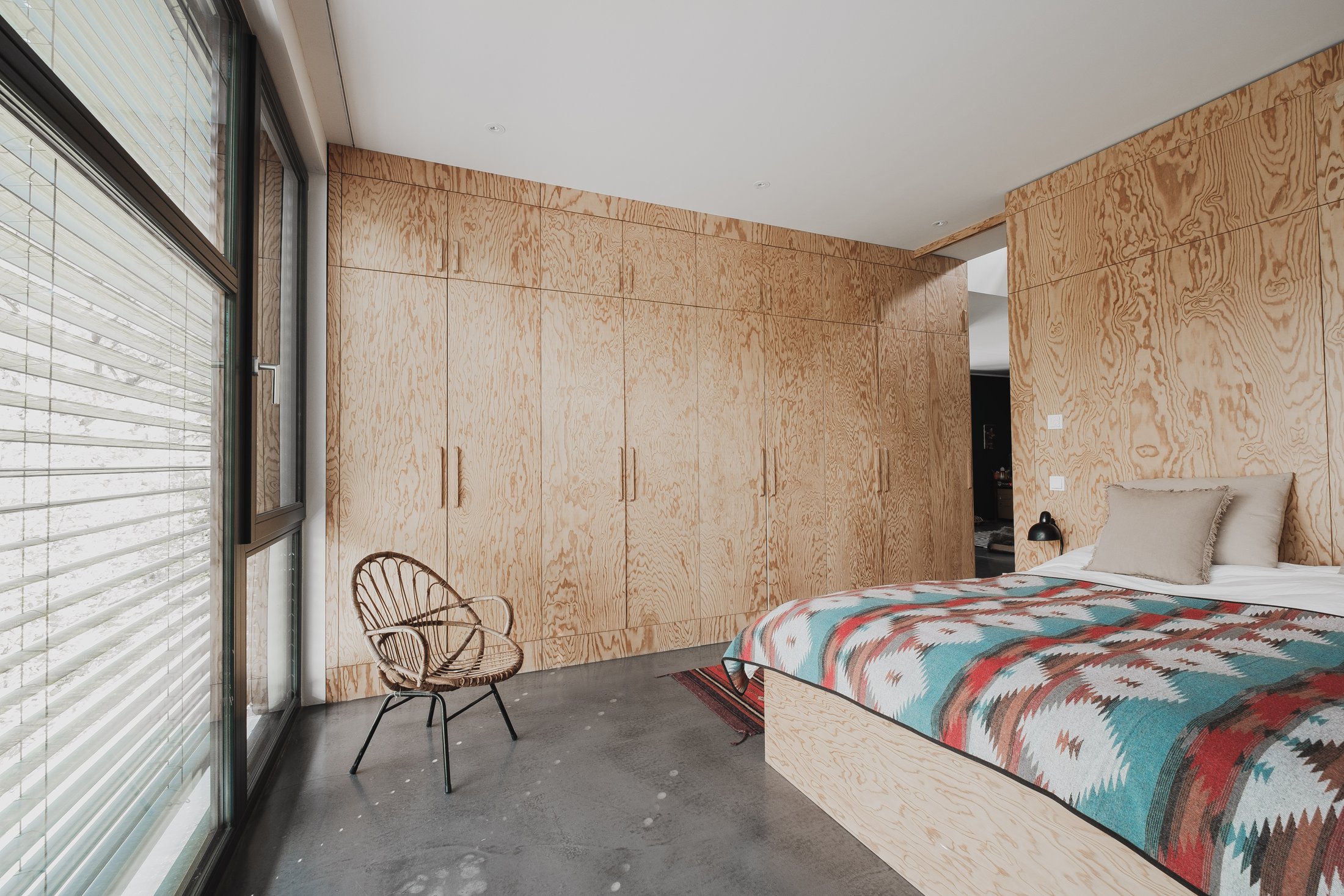 Schlafzimmer mit Holzeinbauschränken, Kelim-Bettdecke und Fensterfront, Das schwarze Haus