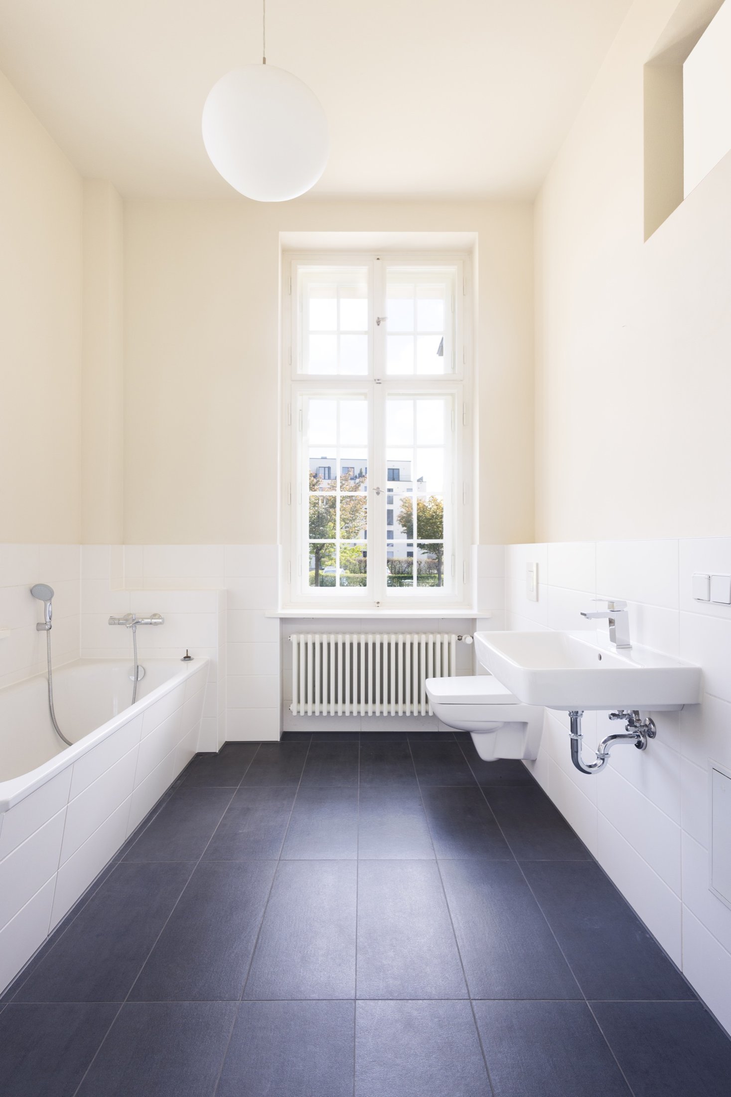 Bad mit Badewanne, hohem Sprossenfenster und dunklem Fliesenboden, Projekt Schütze Immobilien
